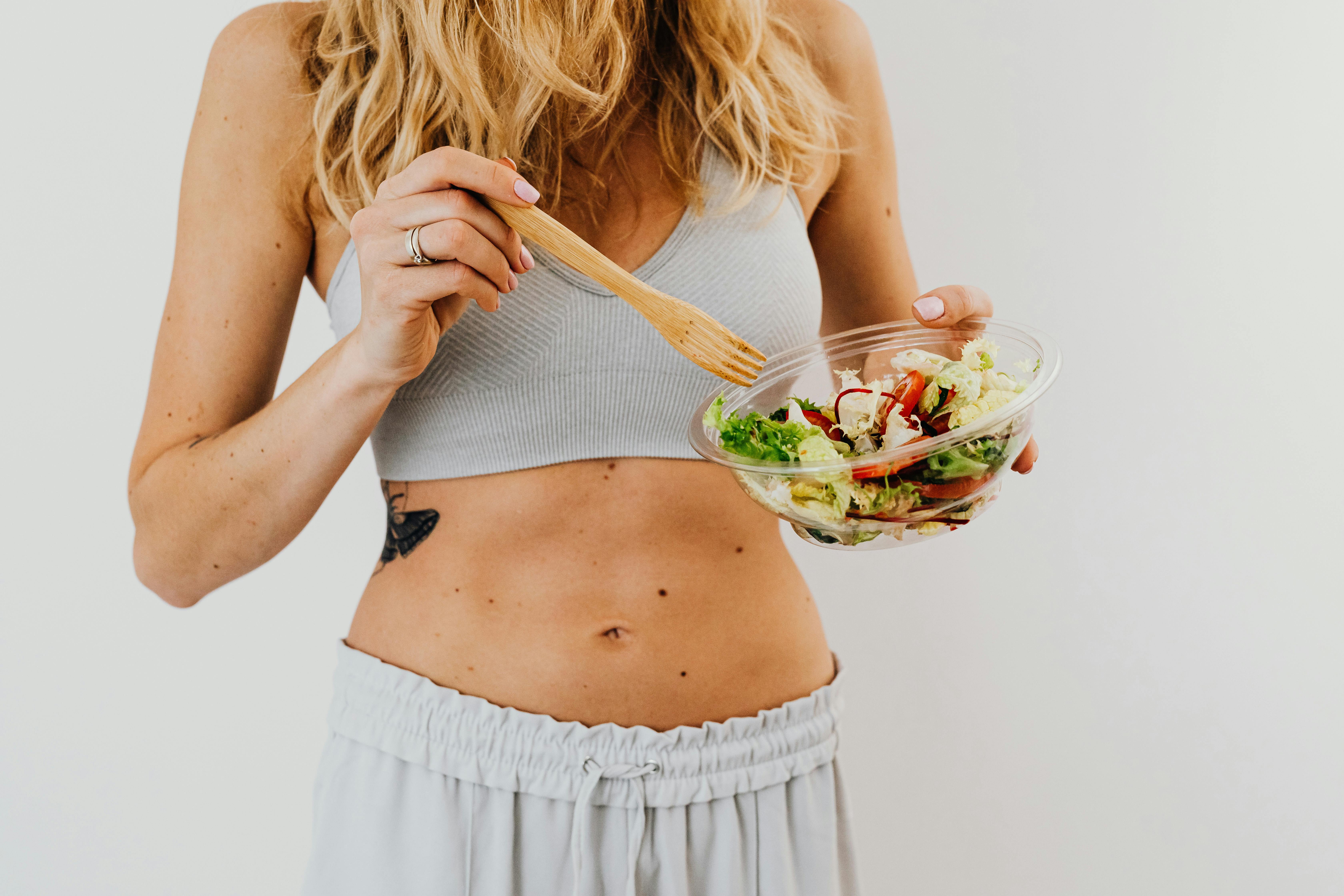 A woman holding a bowl of salad and a wooden fork.