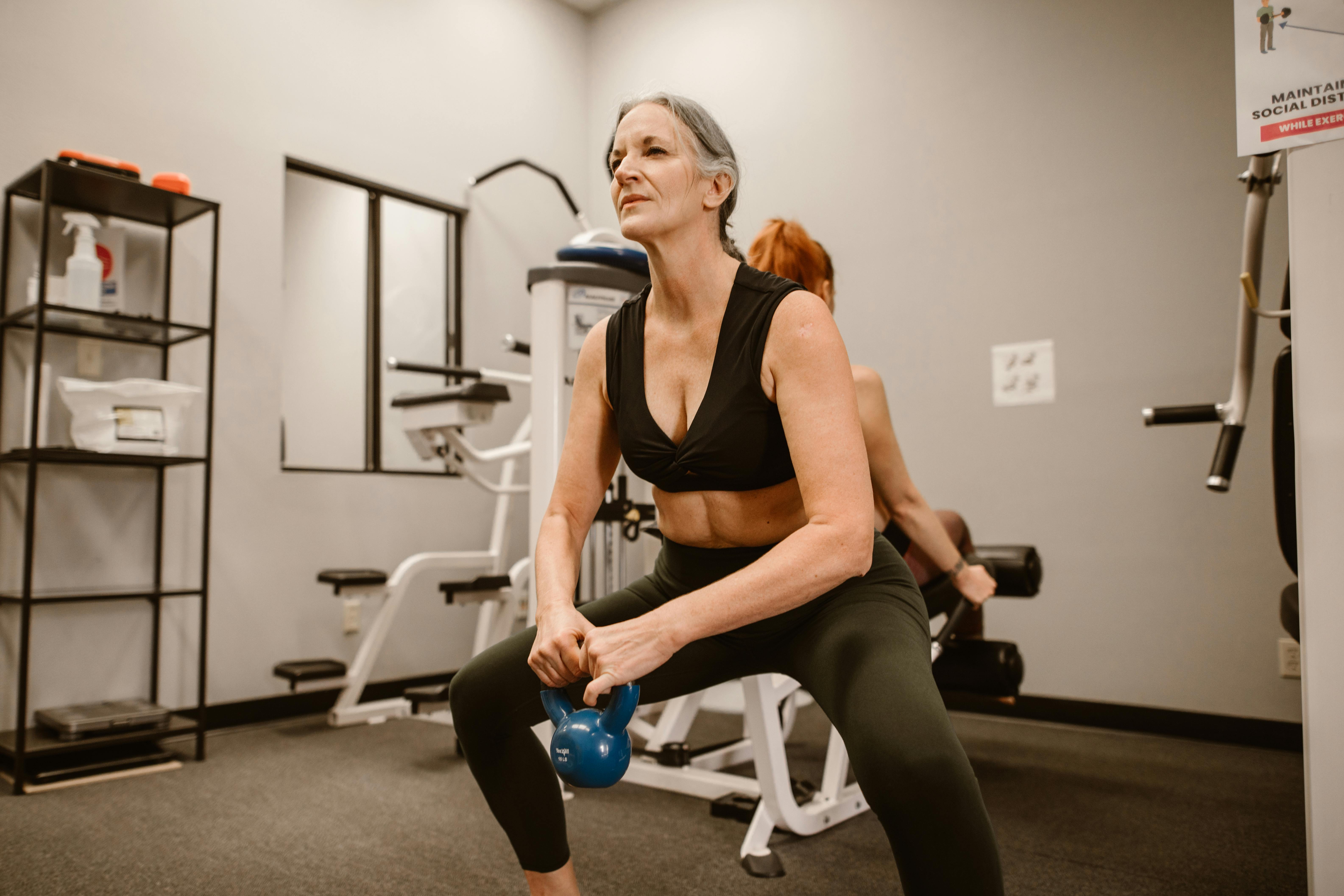 Woman exercising with a kettlebell in a gym setting.