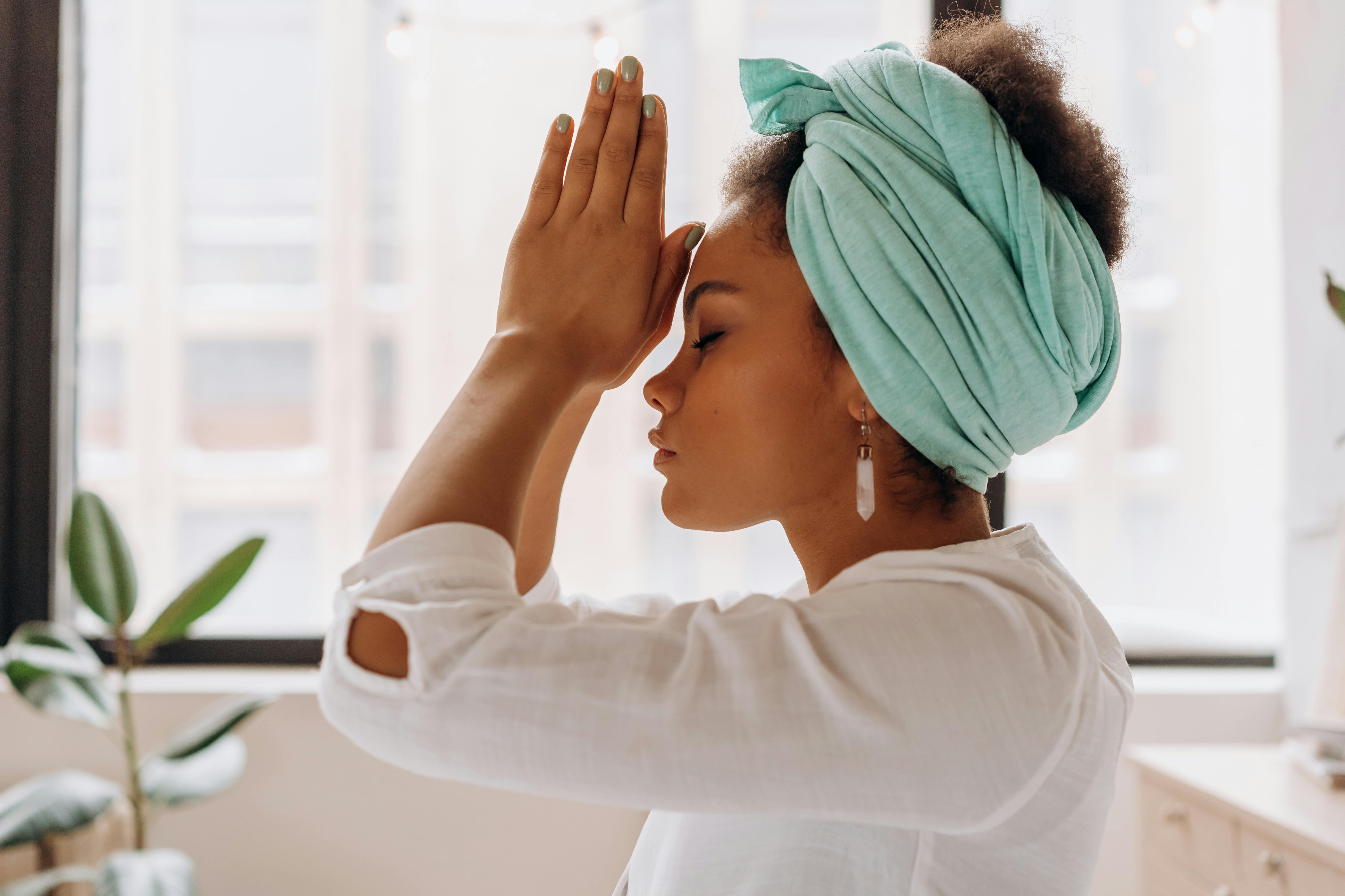 A woman with a light blue headscarf meditating with her hands pressed together