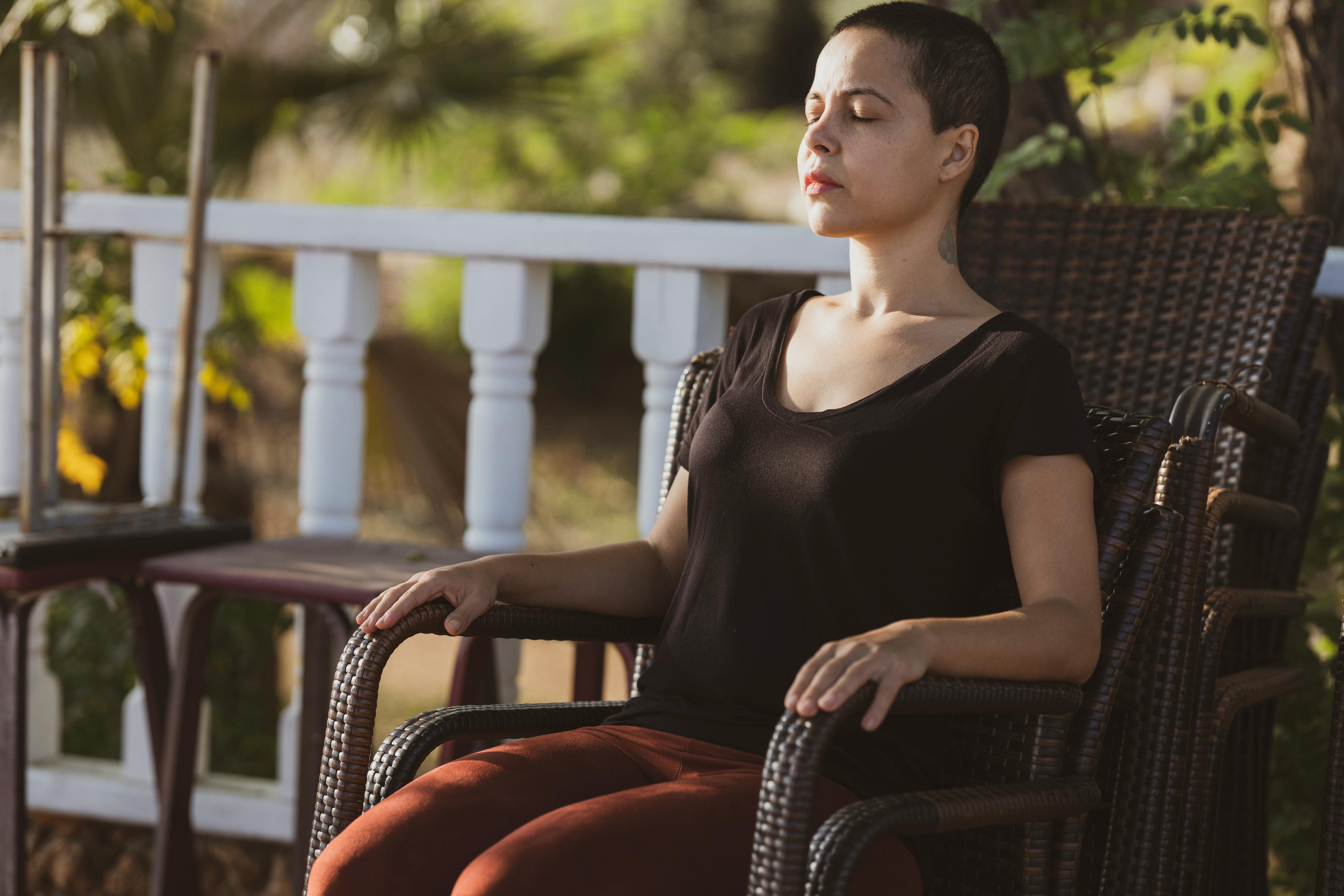 Woman with short hair sitting in a chair, eyes closed, enjoying the sunlight.