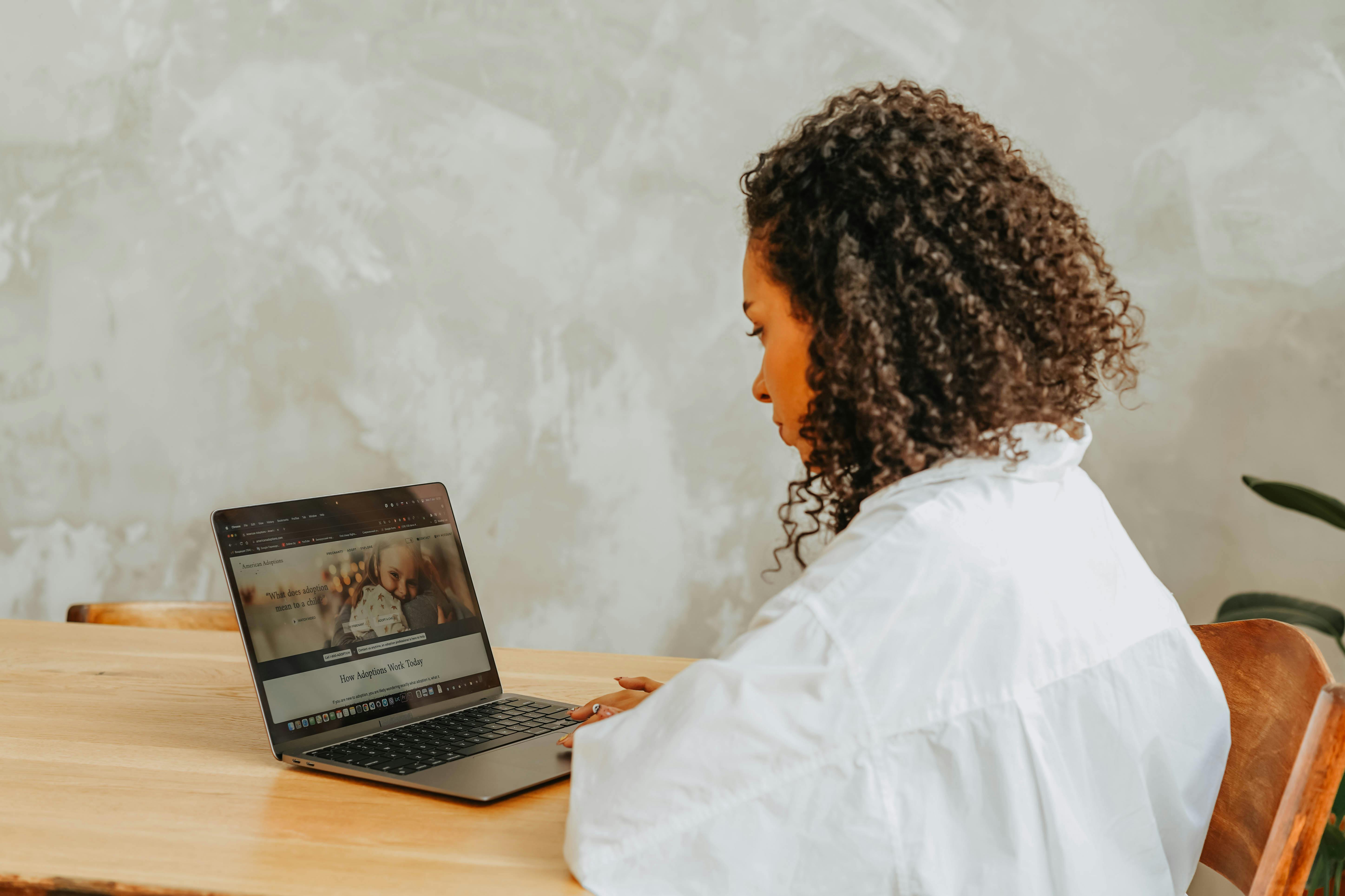 Woman with curly hair working on a laptop at a wooden table.