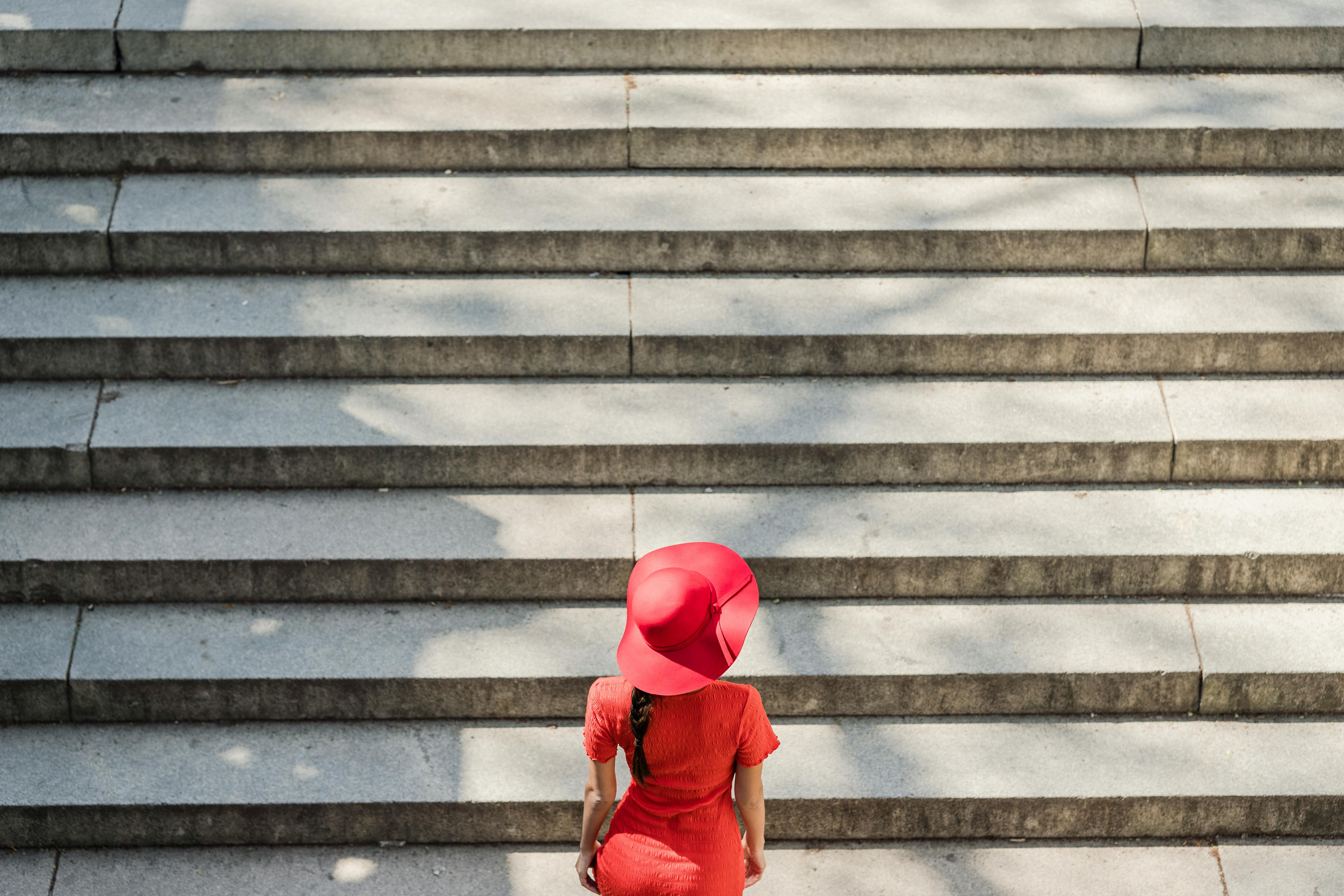 Woman in a red dress and wide-brimmed red hat standing on a staircase