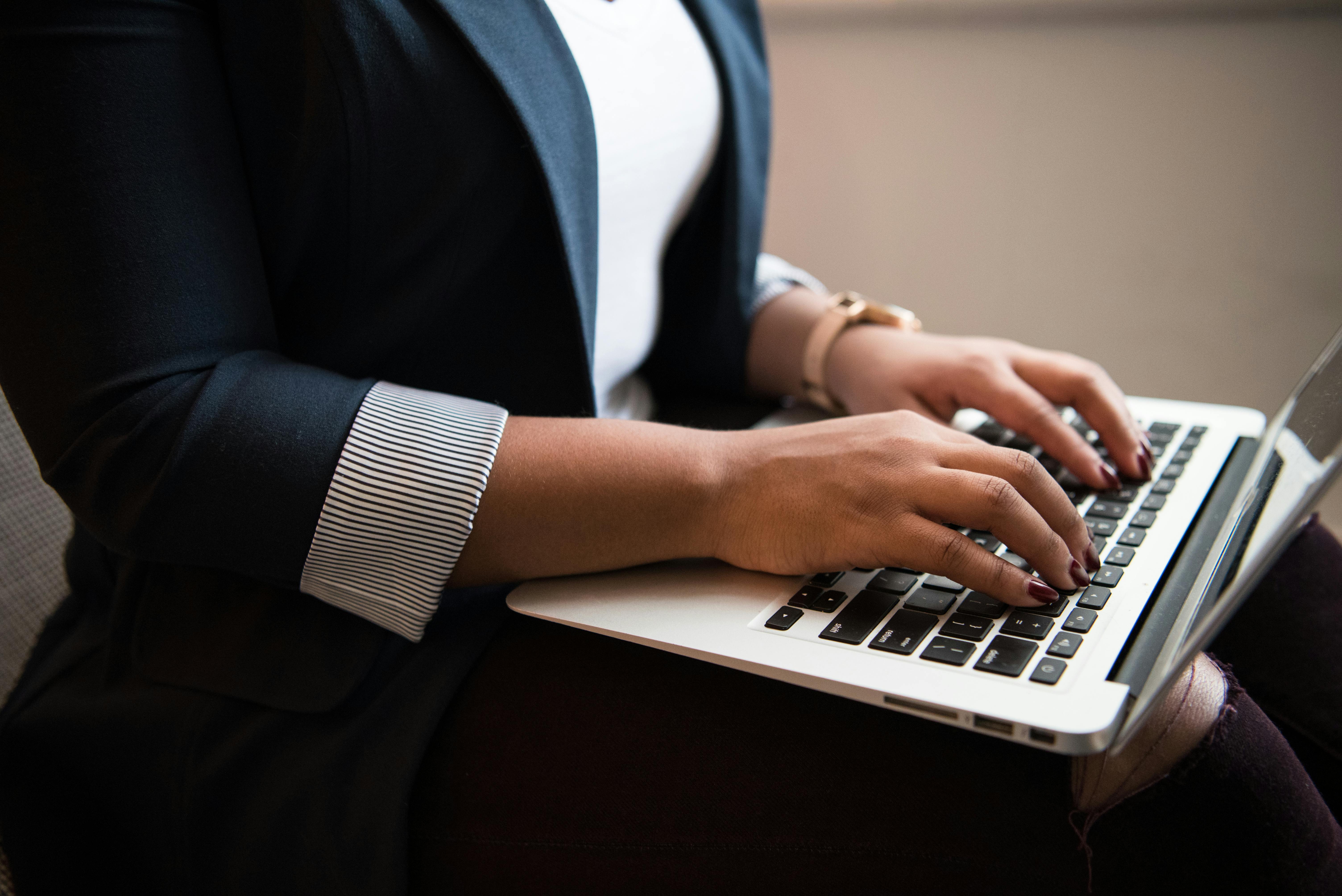 Close-up of a woman's hands typing on a laptop keyboard while sitting.