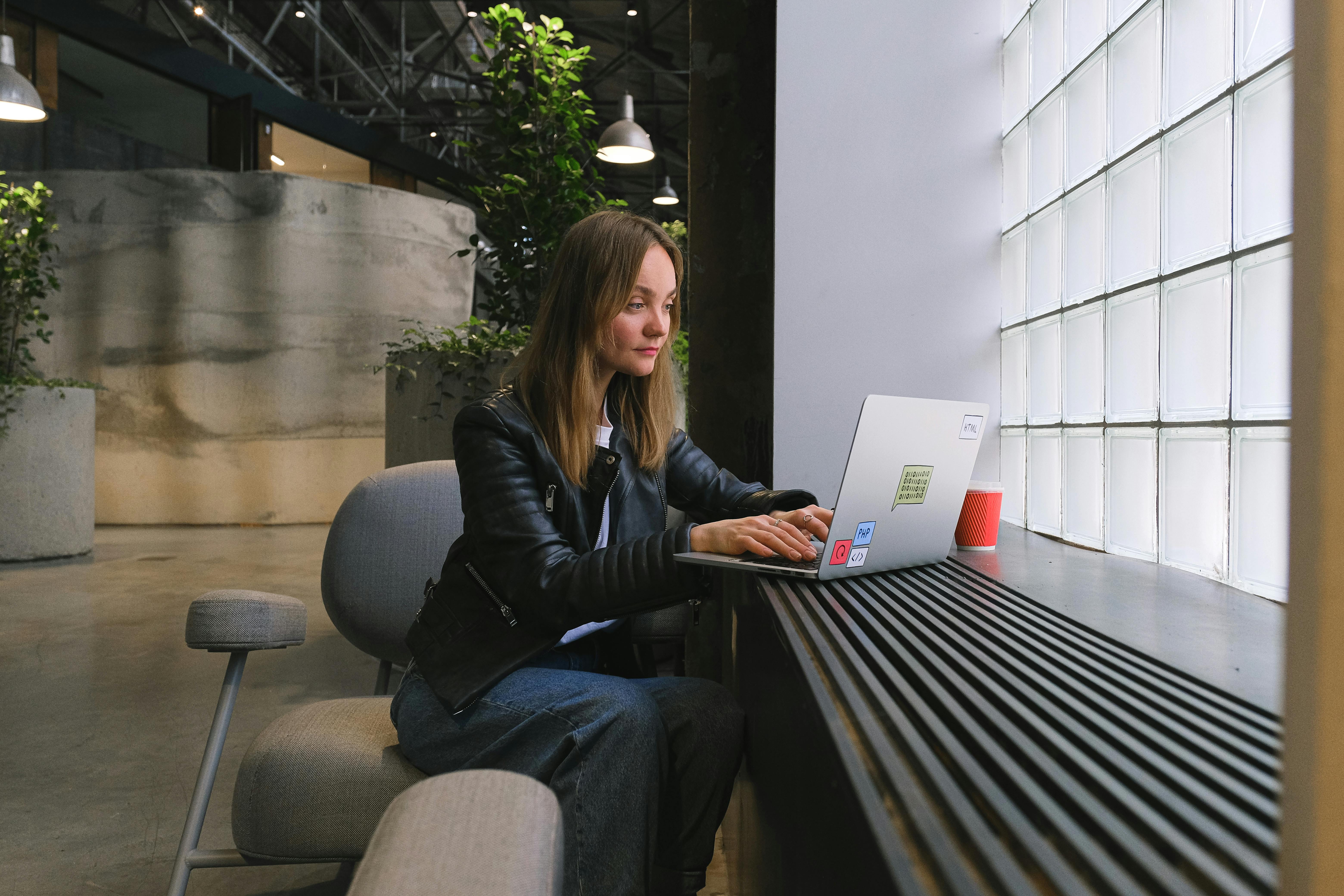 A woman typing on a laptop at a stylish workspace by a window.