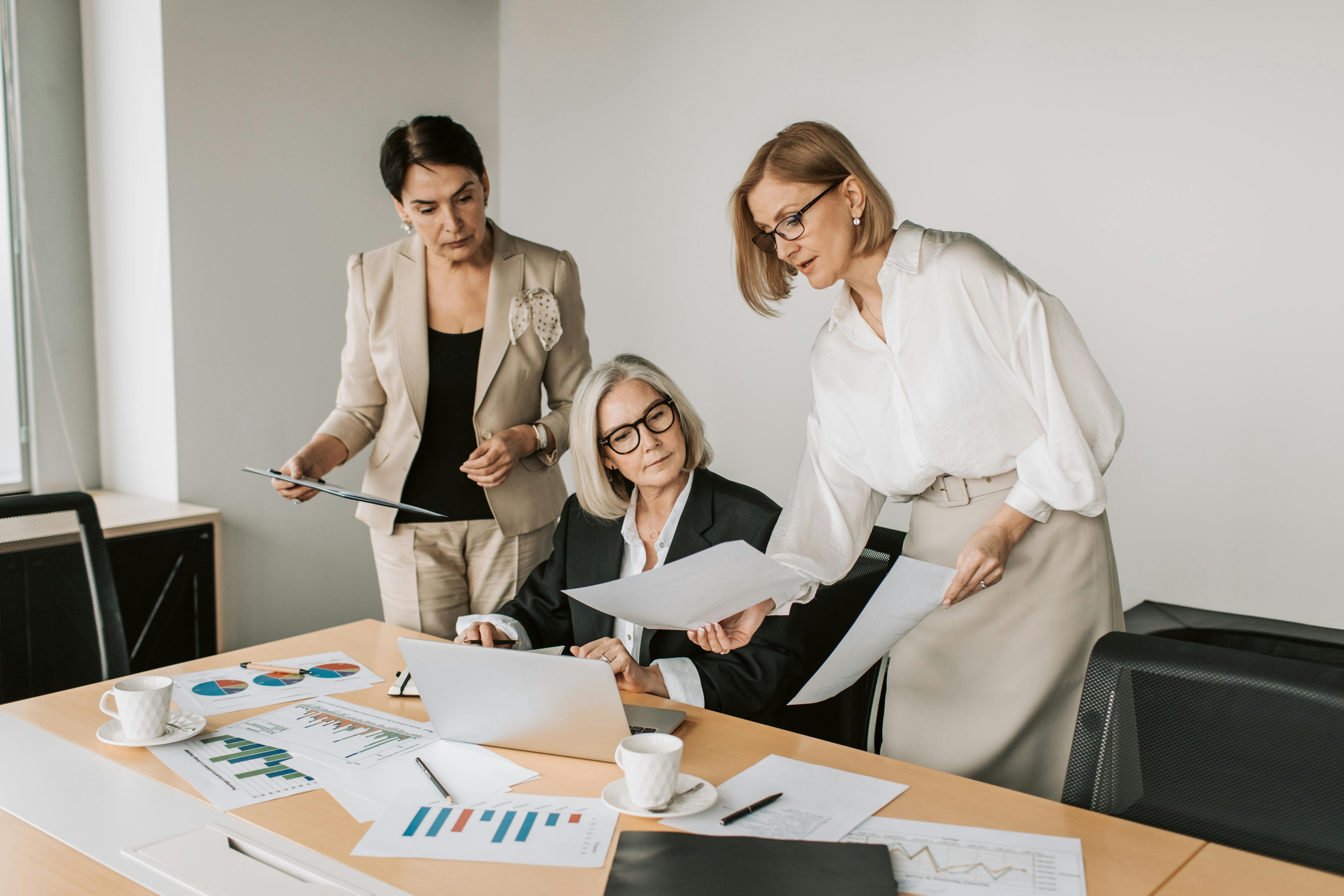 Three professional women discussing documents in a modern office setting.