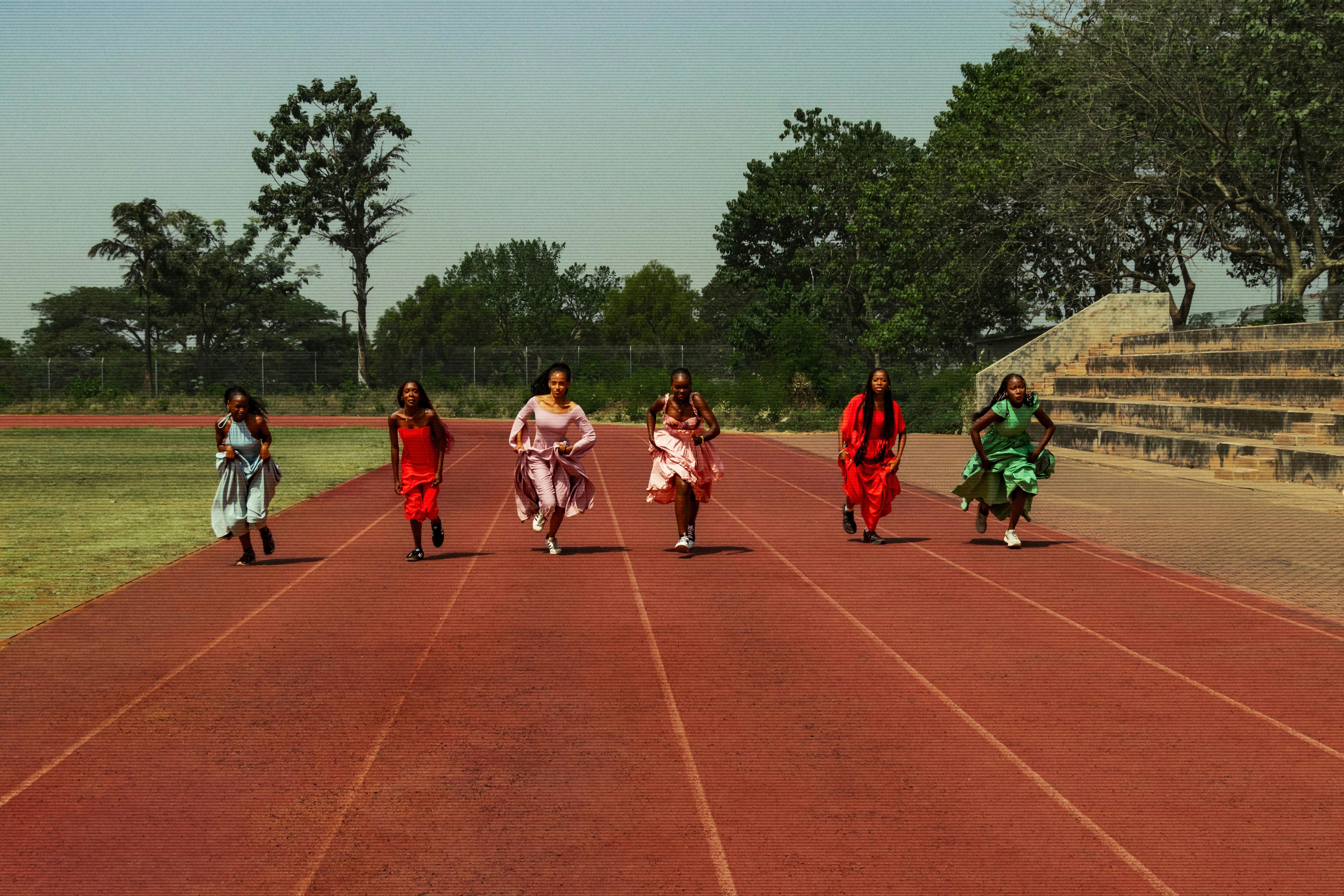 Six women in colorful dresses running on a racetrack