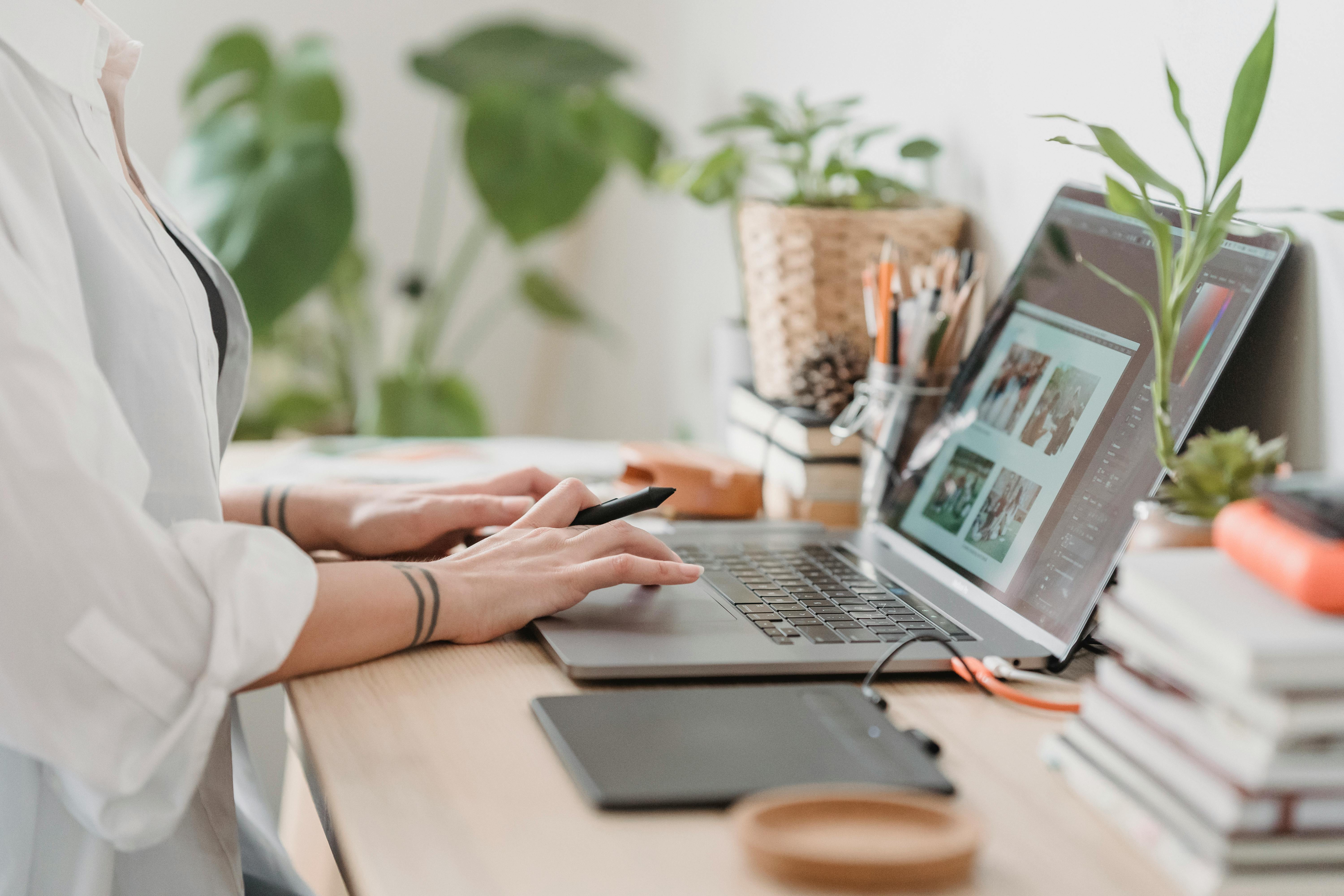 A person working on a laptop at a desk with plants and stationery around.