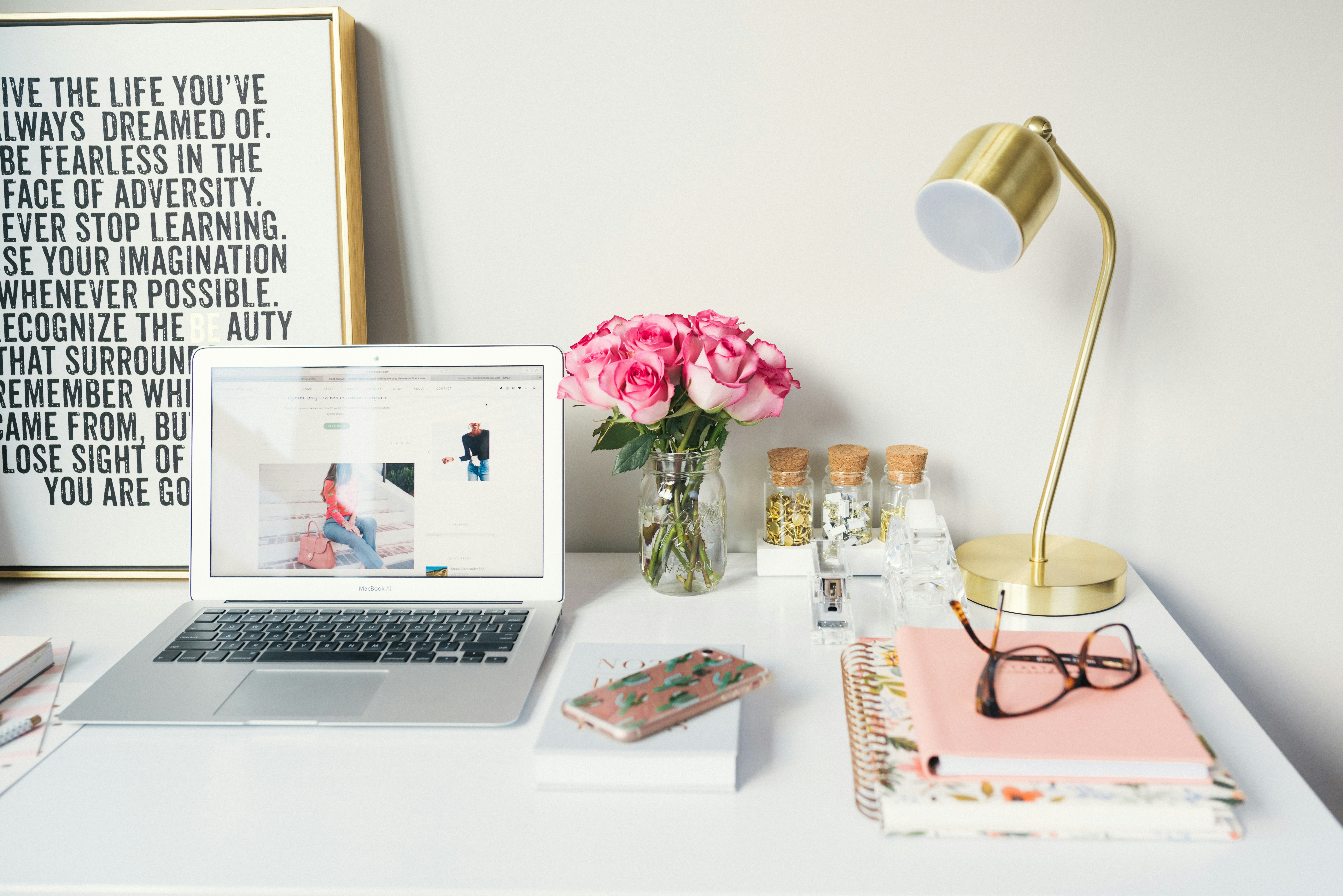 A bright workspace featuring a laptop, a vase of pink roses, and various stationery items.