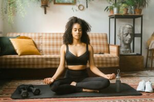 A woman meditating on a yoga mat in a cozy living room setting.