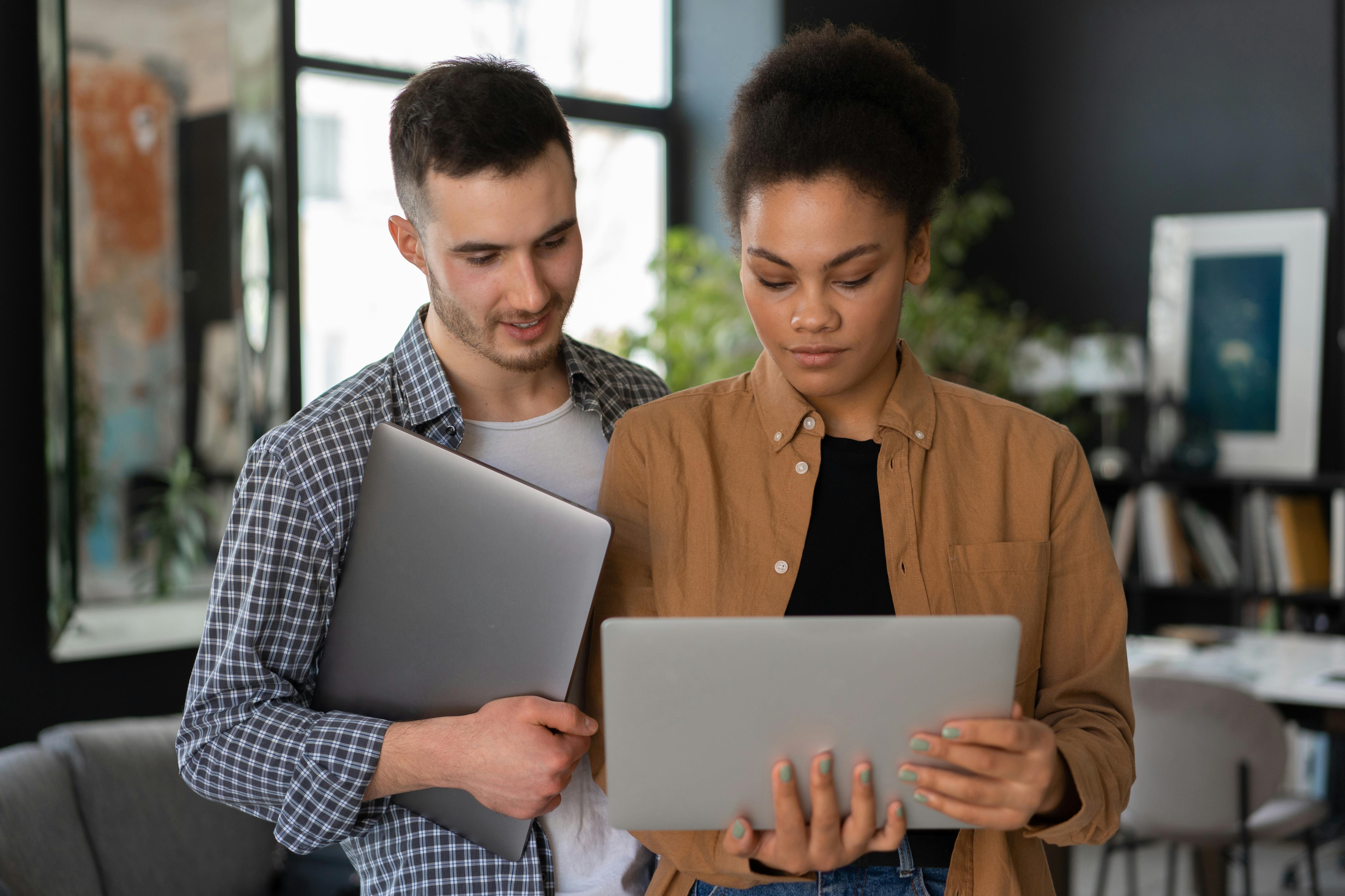 A man and a woman discussing over a laptop in a modern workspace.