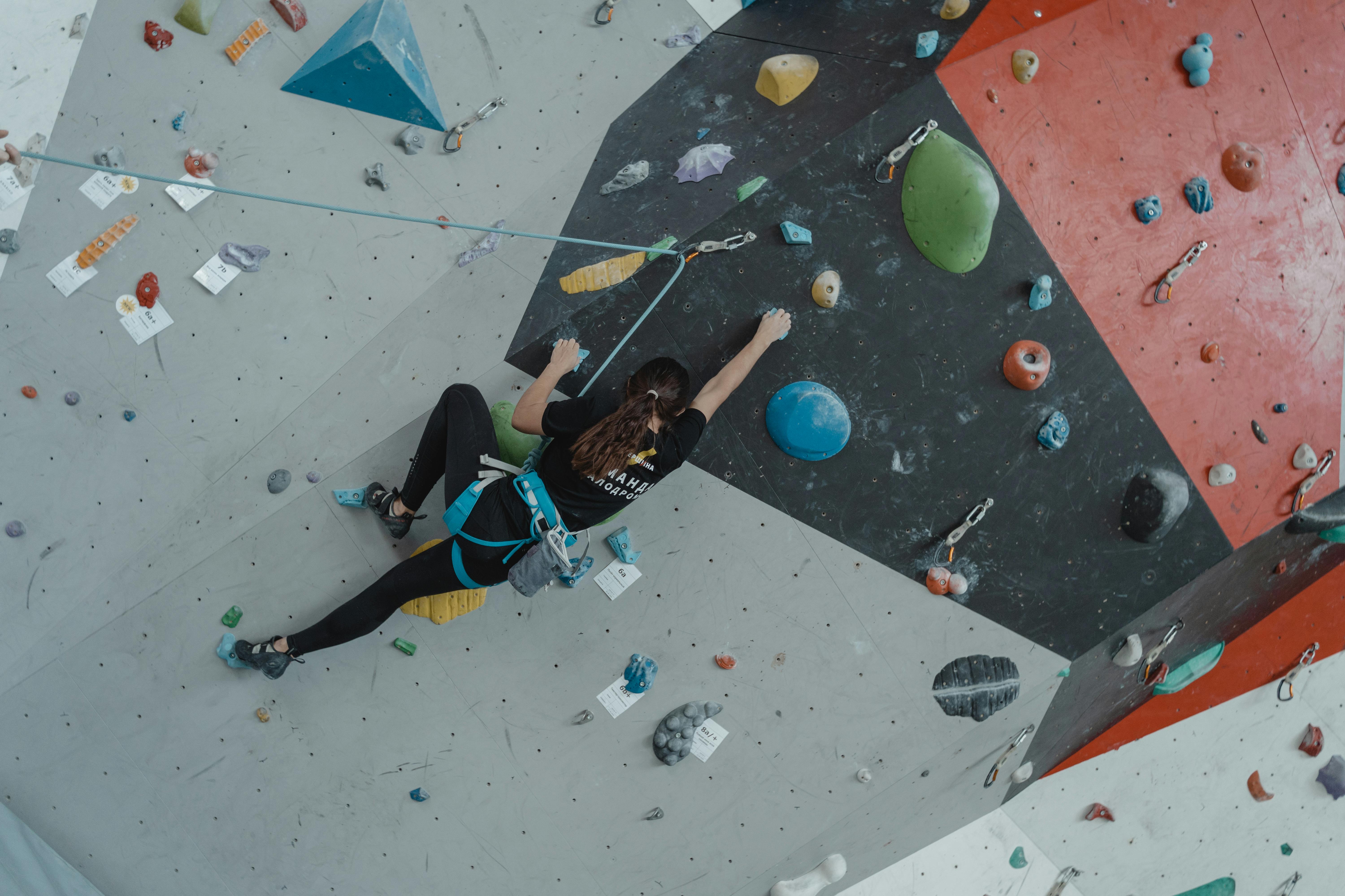 A climber scaling an indoor rock climbing wall with various colored holds.