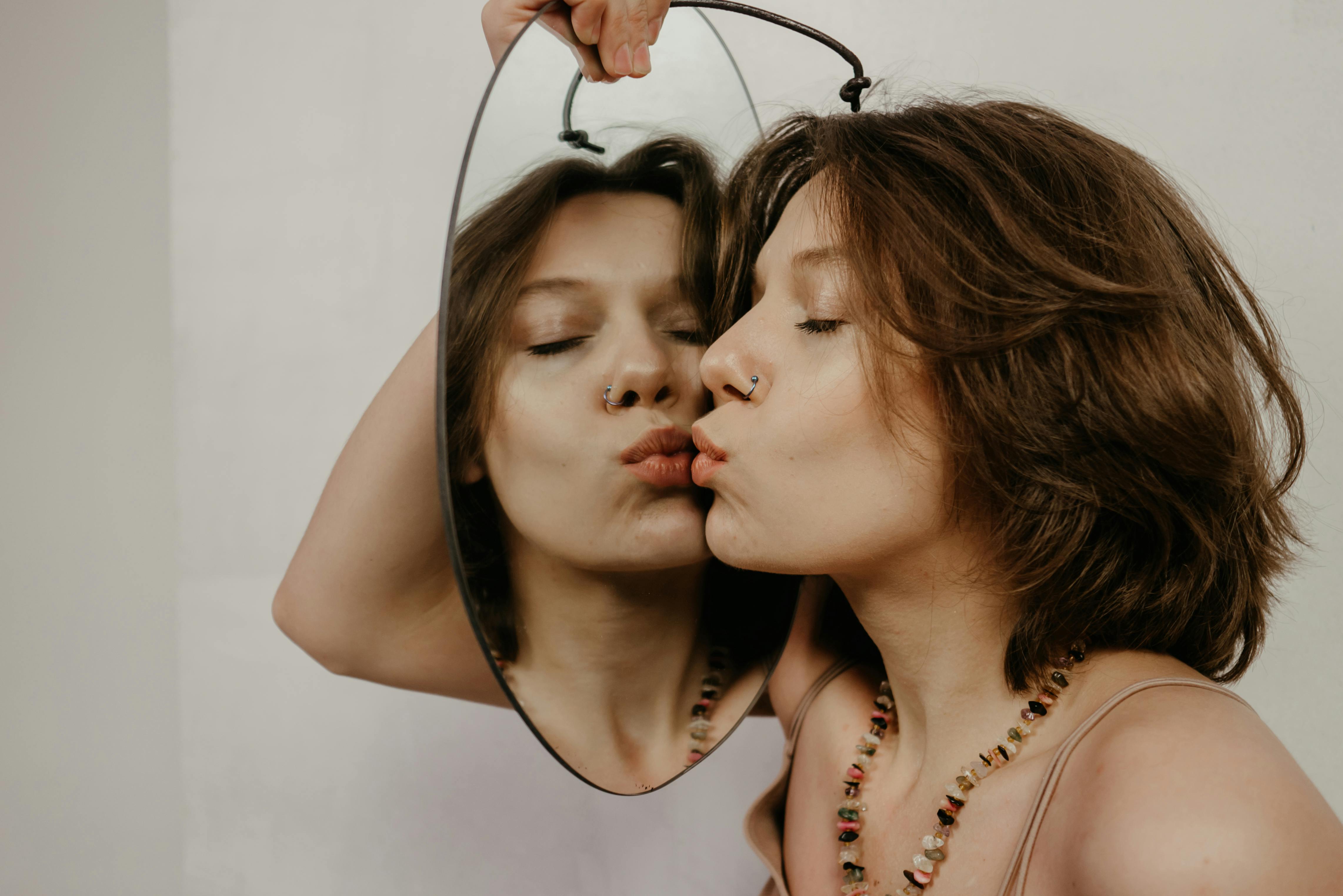 A person holding a mirror while kissing their reflection.