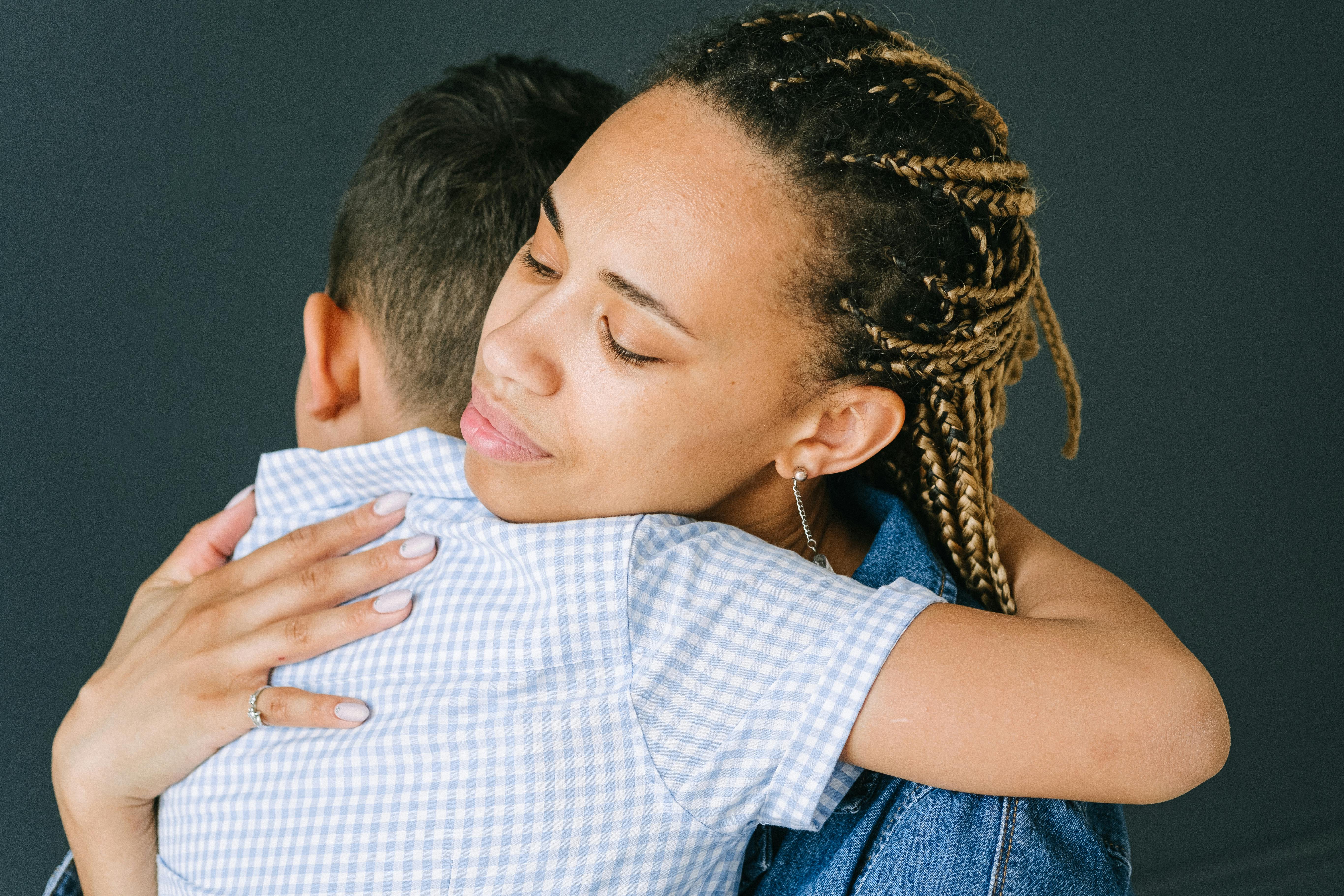 A woman embracing a young child in a tender hug against a dark background.