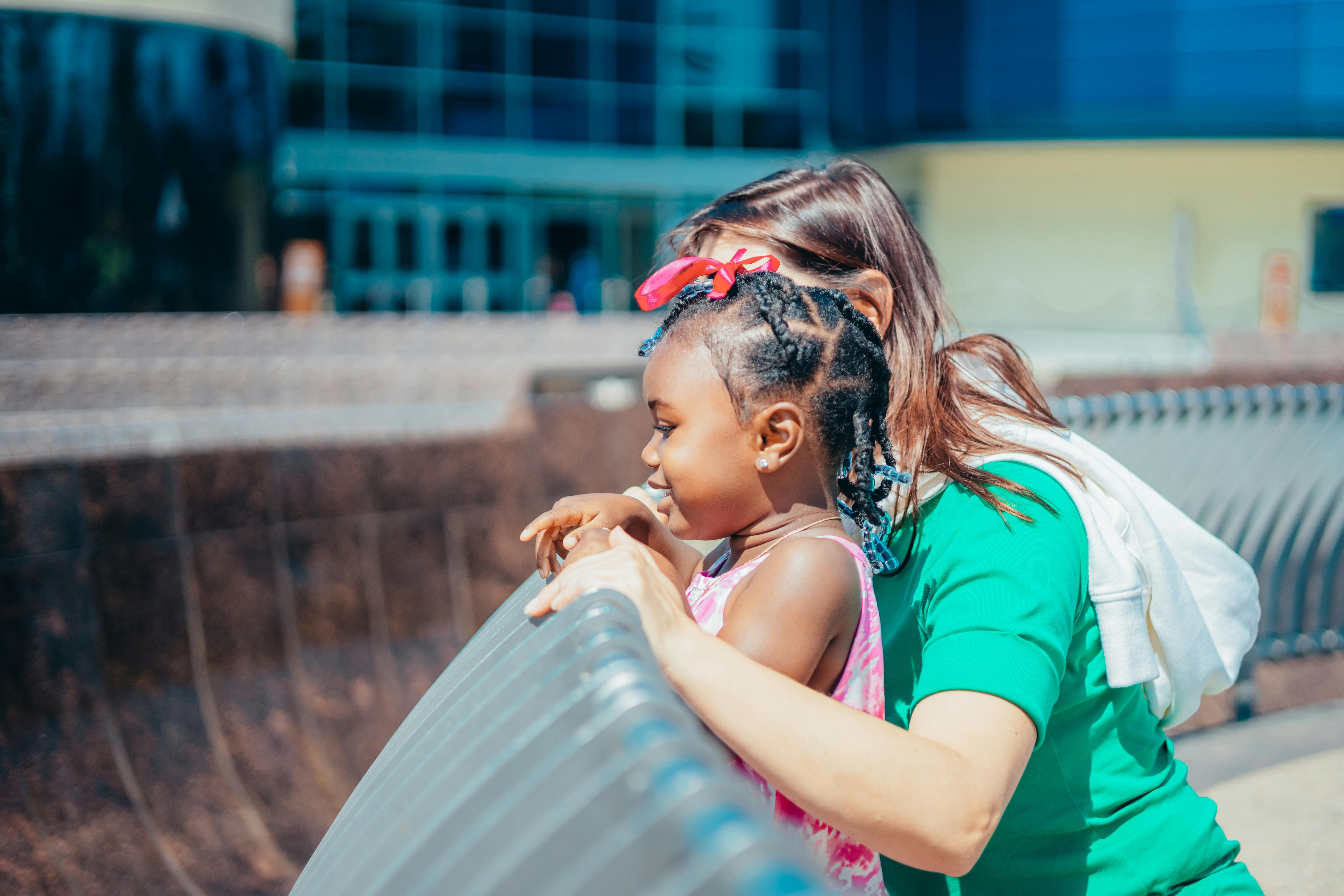 A woman and a young girl enjoying time together outdoors, leaning over a railing