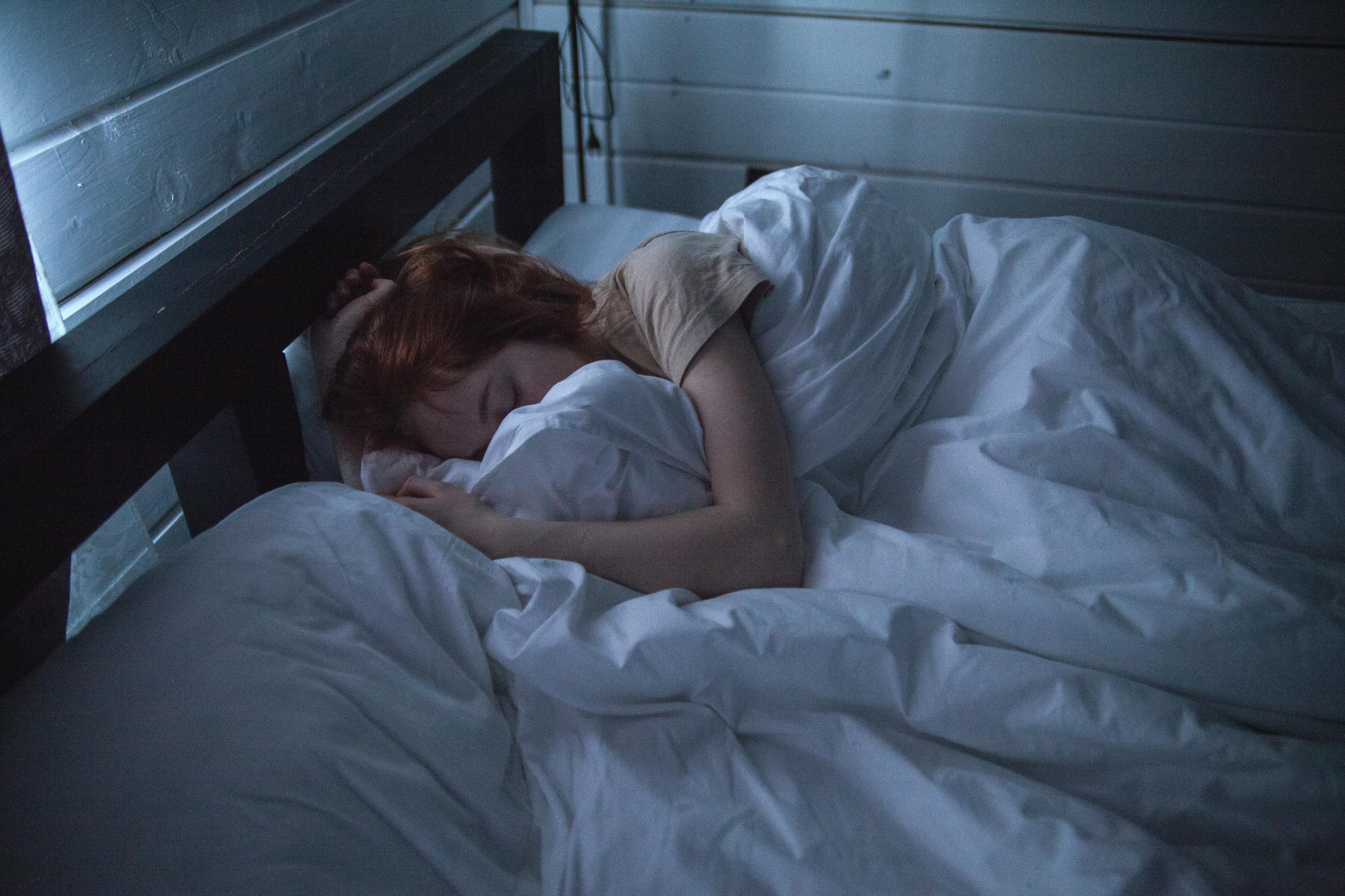 A person with red hair sleeping peacefully under white blankets in a softly lit room