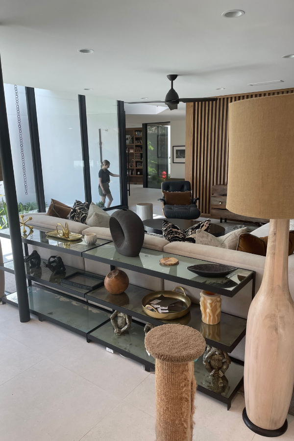 sideboard and lamp in front of large windows in a living room with woman entering doorway