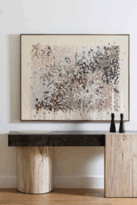 Console table made of light wood and dark stone beneath a large abstract painting in warm muted tones. Designed by April Littmann