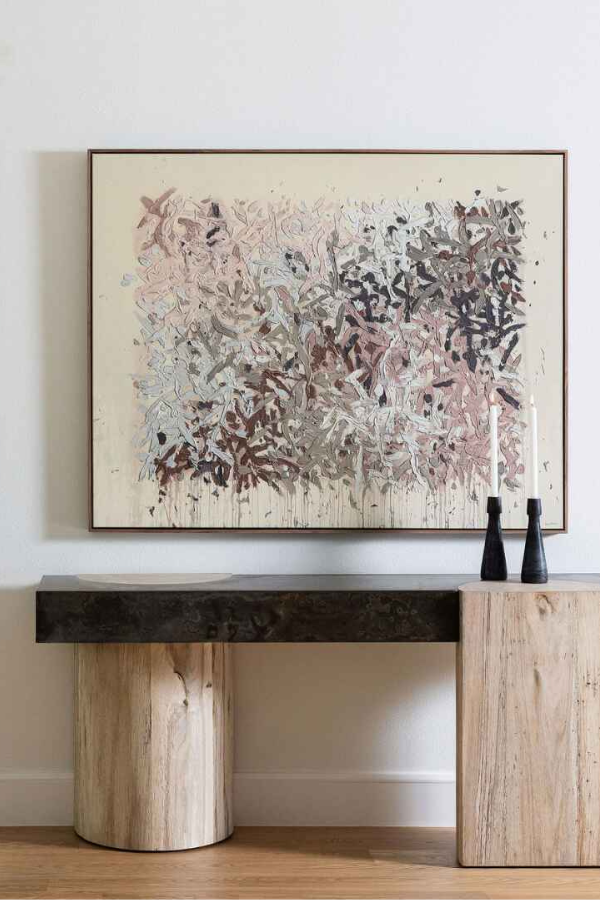 Console table made of light wood and dark stone beneath a large abstract painting in warm muted tones. Designed by April Littmann