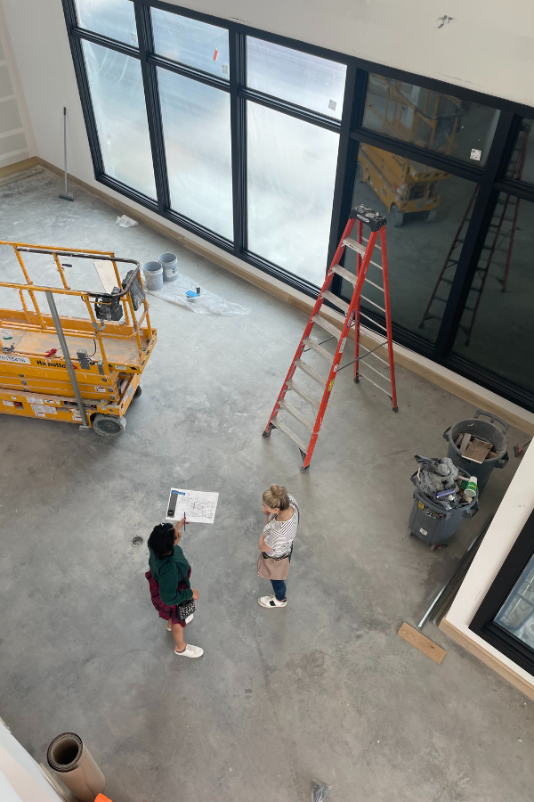 Designers standing on a construction site reviewing plans inside a large open interior space.