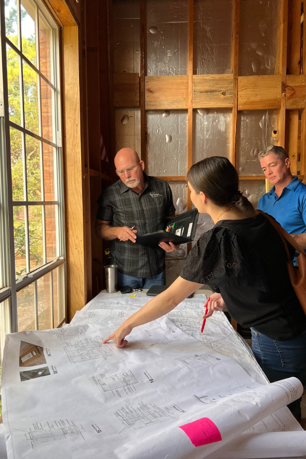a designer indicating progress on a plan at a client's home with two contractors