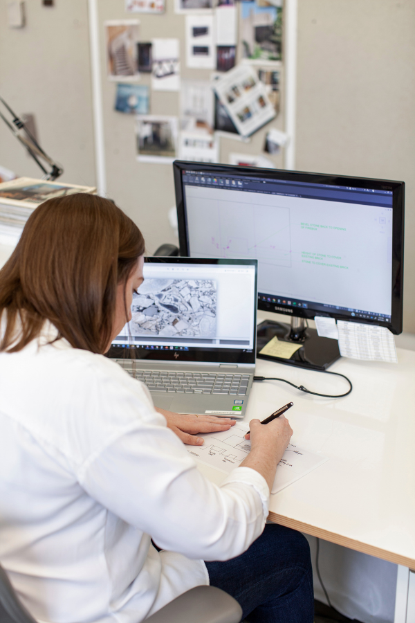 a designer sits at her desk writing and using a laptop