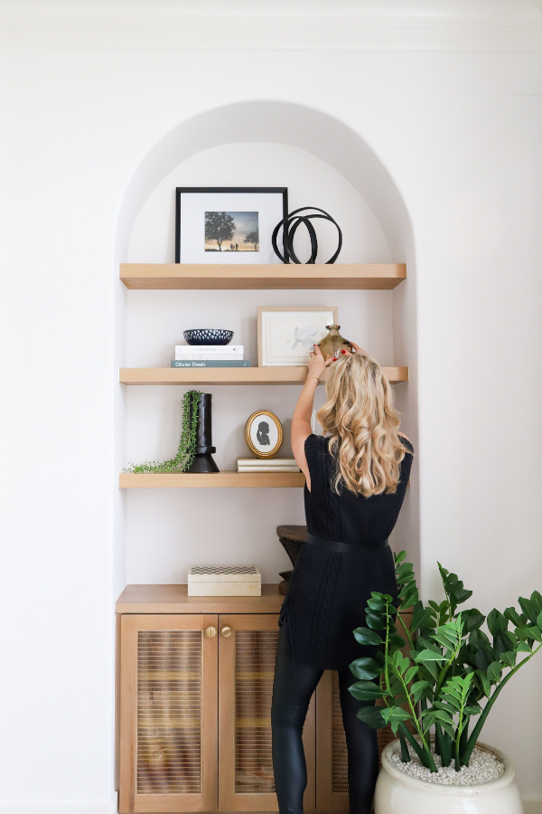 a designer arranges objects on shelves in a client's house