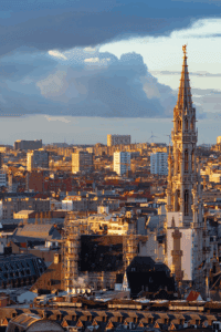 Brussels cityscape at golden hour with the Gothic tower of Brussels Town Hall rising above historic rooftops.