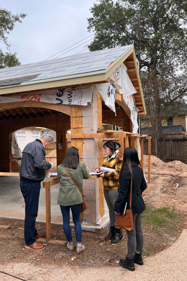 Design team members and project partners review plans together at a residential construction site during the framing stage.