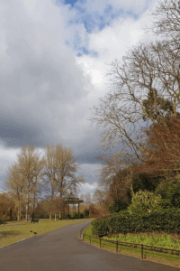 A curving path through Regent’s Park beside landscaped flower beds and leafless trees, beneath dramatic grey-and-white clouds.